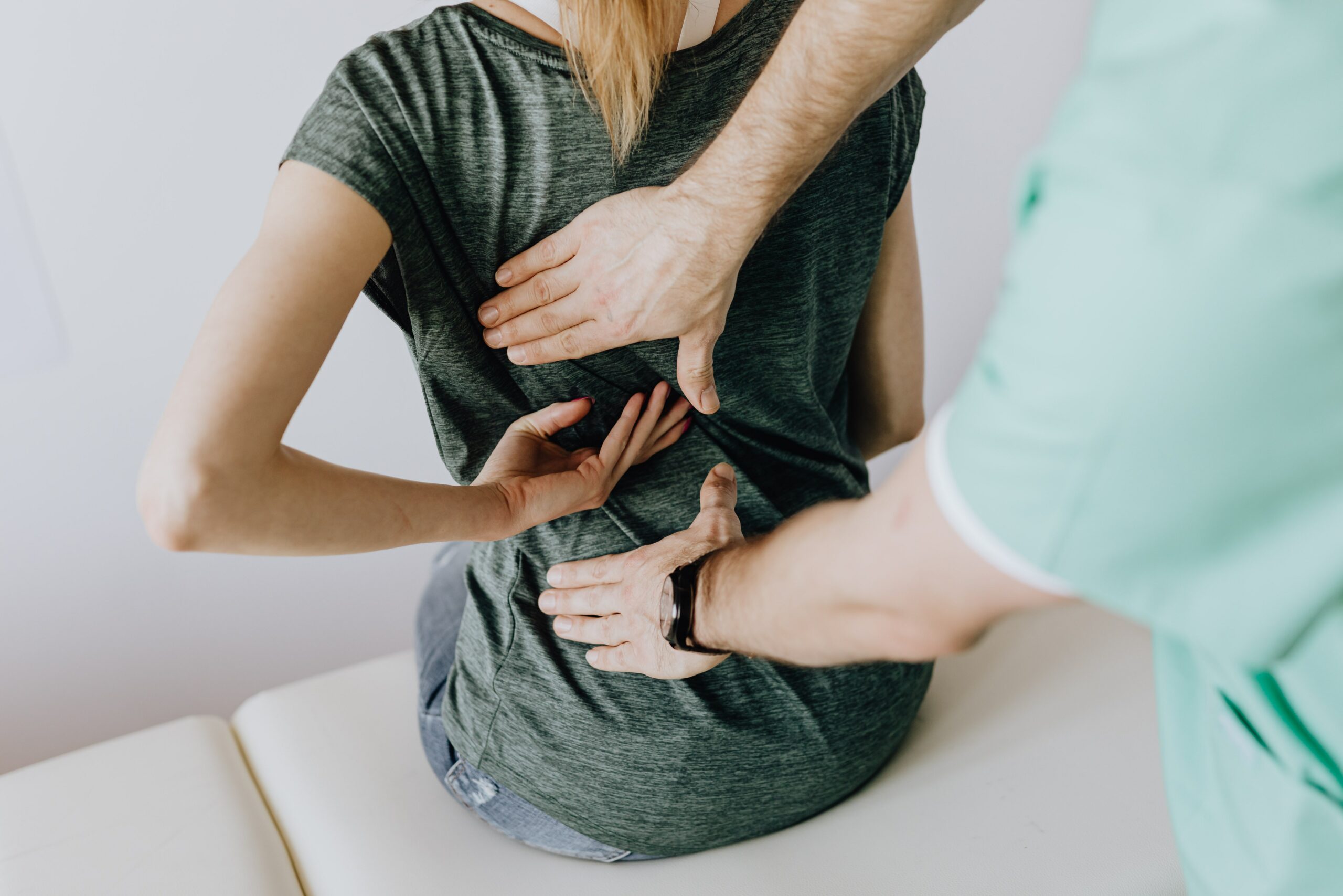 woman sitting with back pain, and doctor standing behind her feeling her back