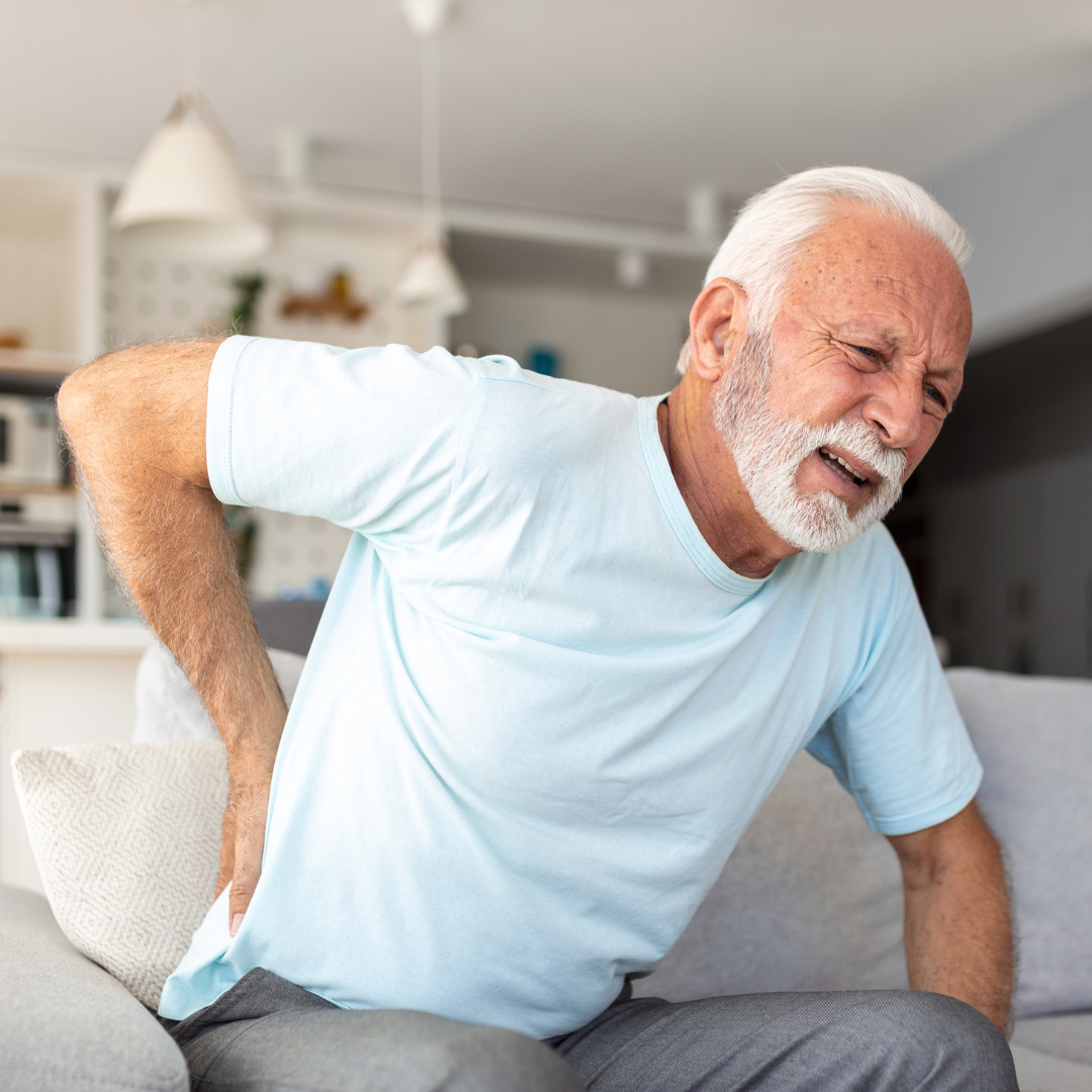 senior male sitting on couch with severe back pain and sciatica